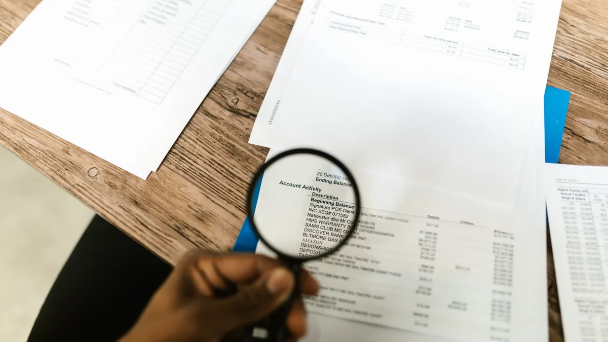 Hands using a magnifying glass over paperwork to inspect details